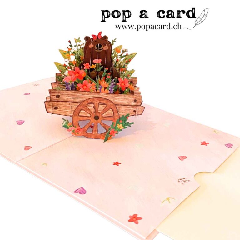 Open 3‑D card shows brown bear in wooden cart overflowing with pastel blooms