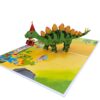 Angled view of the open 3D pop-up birthday card with a stegosaurus in a party hat and little dinosaurs
