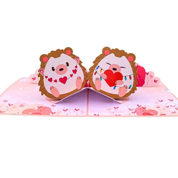 Angled view of the open 3D pop-up love card with two hedgehogs, a heart garland and fairy lights